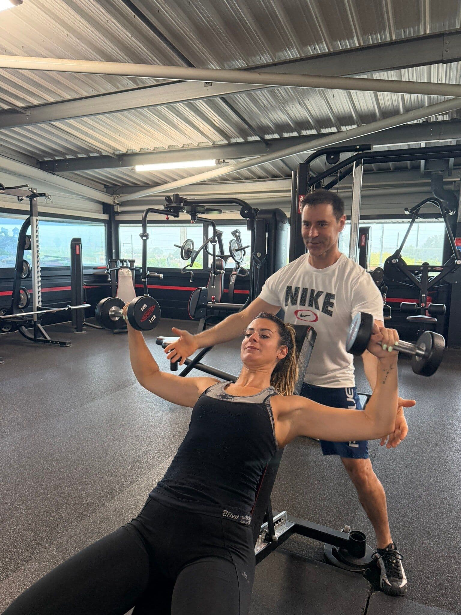 Un coach guide une adhérente pendant un exercice de musculation sur une machine guidée.